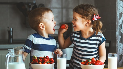 Deux très jeunes enfants s'amusent avec des fraises, en rigolant